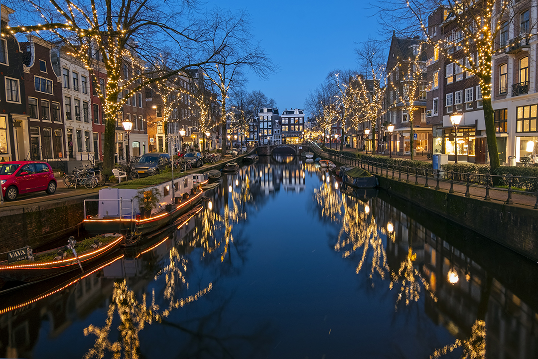 Christmas lights reflecting off canal with shops and houses either side of the bank at night in Amsterdam